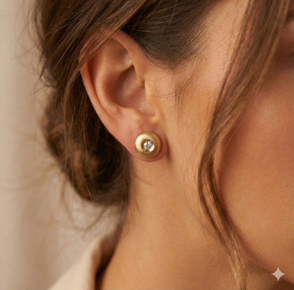 Nainen käyttää mattapintaisia kultaisia timanttikorvakoruja