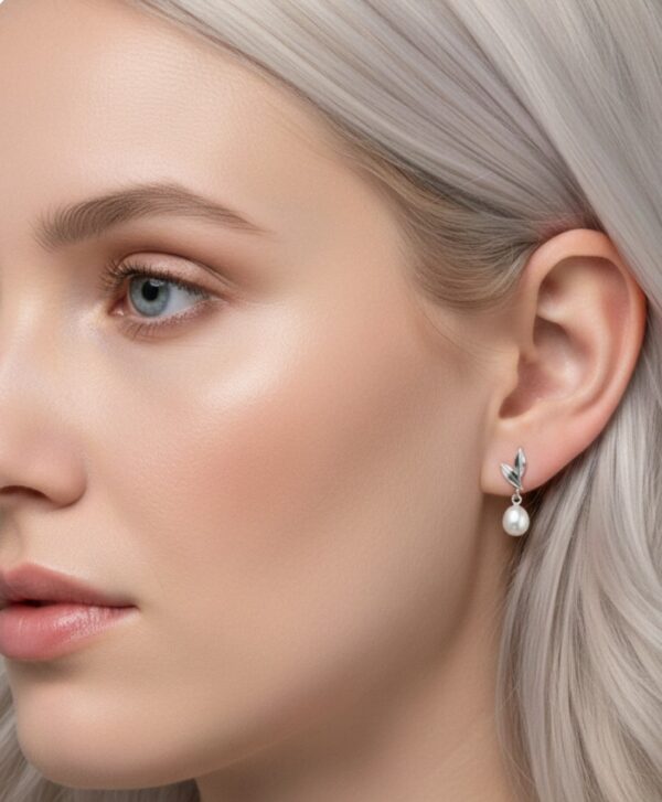 Valkokultainen korvakoru ja makean veden helmi naisen korvassa.