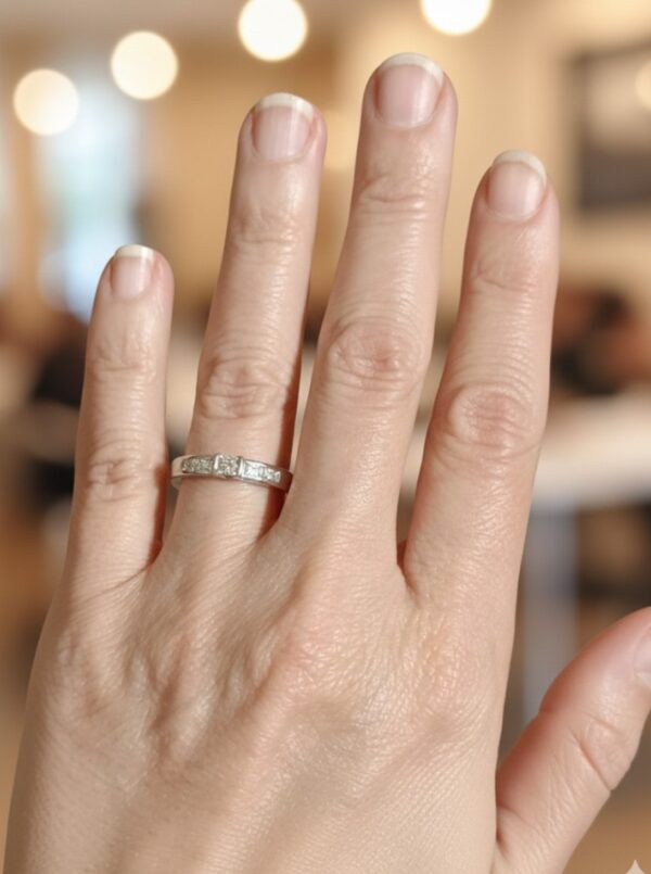 Kädessä valkokultainen timanttisormus, jossa princess-hiottu keskikivi ja briljanttisivukivet.